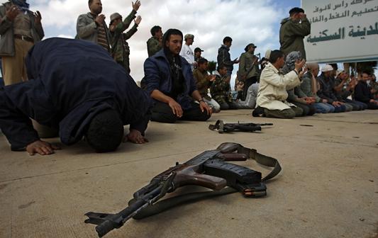 Rebel fighters pray at the gate to Ras Lanuf, a center for oil production that was hit by several airstrikes from forces loyal to Libyan dictator Muammar Qaddafi, Tuesday, March 8, 2011. 