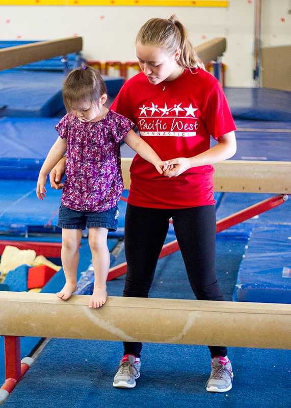 Pacific West instructor helps a young member on the balance beam.