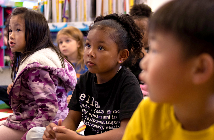Kindergarten is the first year for children to learn the behavior expected in school. Phoebe (left), age 5, and Nala (center), age 5, listen attentively to their teacher at the front of the room.