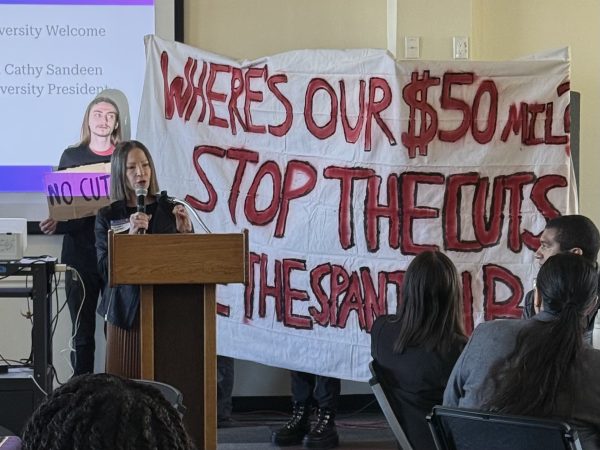 Demonstrators from Students for Quality Education raising a banner behind CSUEB President Cathy Sandeen during the HSI Summit on March 5. The banner reads: “Where’s our $50 mil? Stop the cuts. Save the Spanish B.A.” Photo courtesy of Kenia Juárez.